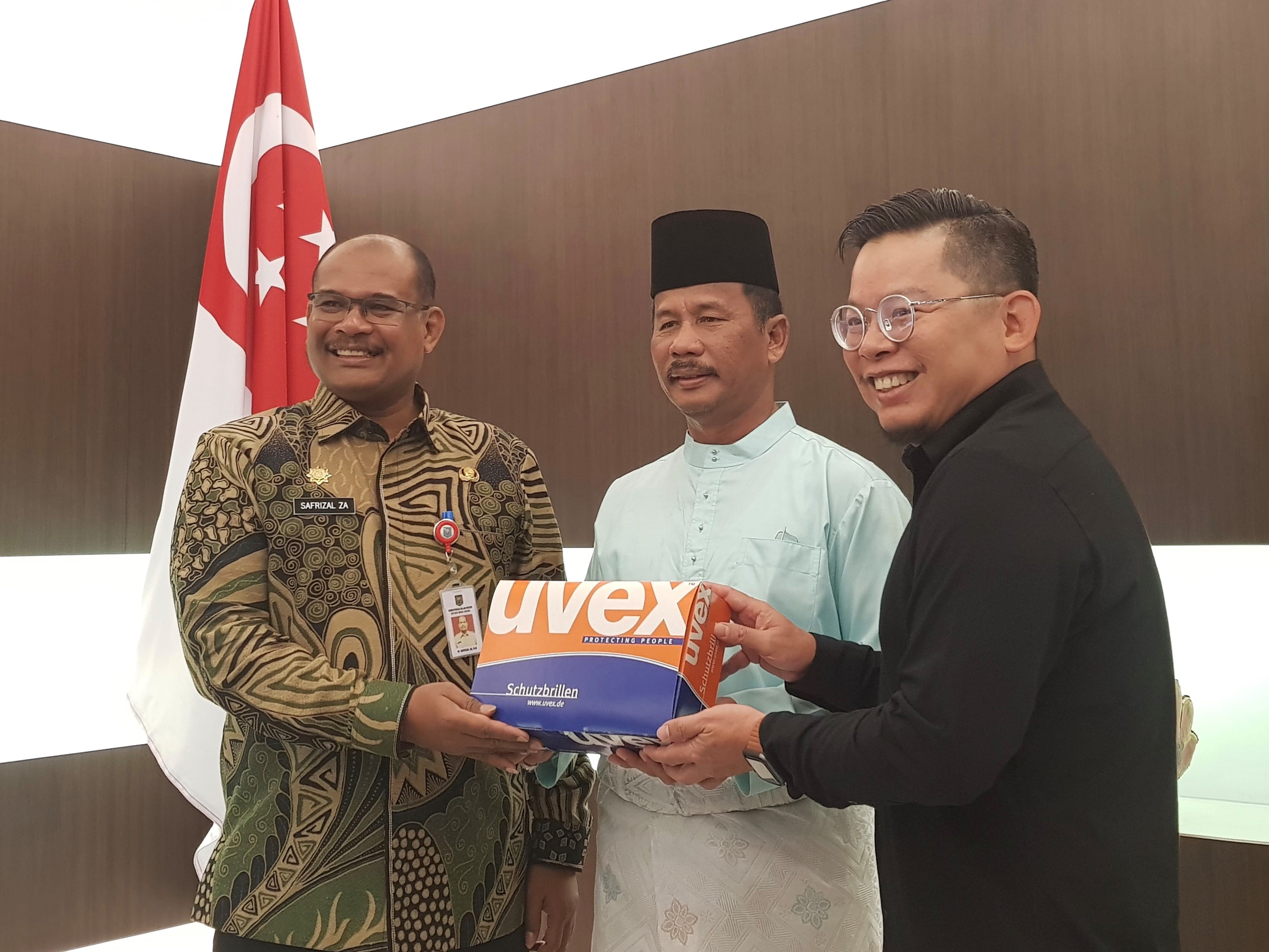Three men with a Uvex box, Singapore flag in the background.